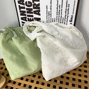 Detailed close-up of textured floral relief on light green and white fabric tote bags