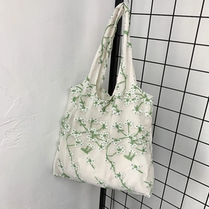 Detail view of delicate green floral embroidery on semi-transparent white mesh tote bag