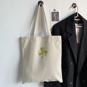 Detail of green clover embroidery on a natural cream canvas tote bag in a stylish setting