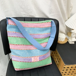 Detail einer bunten gewebten Tragetasche mit blauem Gurt und Handmade-Label auf Stuhl