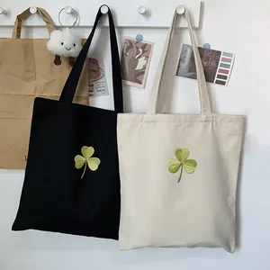 Detail of shamrock embroidery on black and beige canvas tote bags with long handles