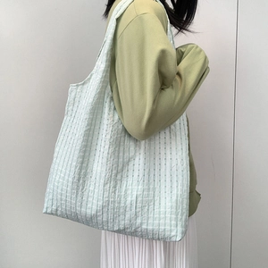 Detailed side view of large mint green checkered canvas tote bag worn by a model