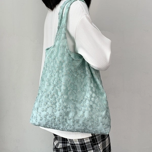 Close-up of mint green mesh tote bag with white daisy embroidery and floral texture