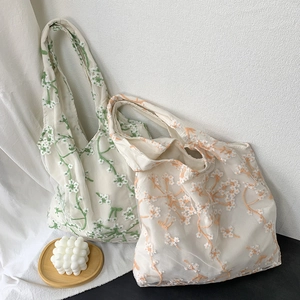 Close-up of green and orange floral embroidery on translucent white mesh tote bags