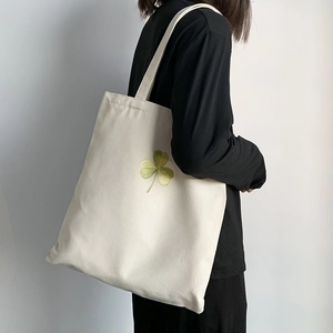 Detailed view of white canvas tote bag with green clover print carried by a model