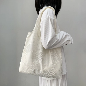 Detail of leaf jacquard texture on minimalist off-white canvas tote bag worn by model