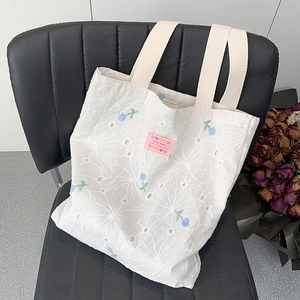 Detailed macro view of white floral hollow embroidery and handmade tag on canvas tote