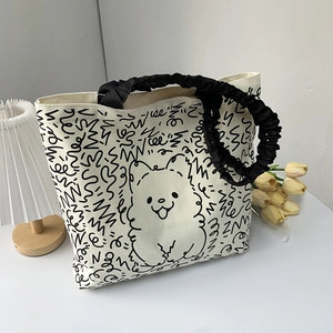 Detail of canvas tote bag with cartoon dog print and black ruffled handle on white desk