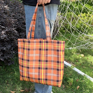 Détail du grand sac cabas à carreaux orange et jaune porté par un modèle à l'extérieur