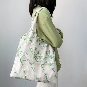 Detail shot of green floral embroidery on white mesh shoulder bag worn with green hoodie