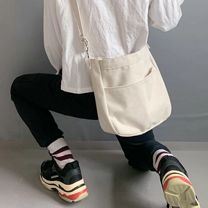 Detail of a beige canvas crossbody bag with front pockets on a minimalist model pose