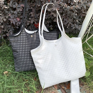 Detail of checkered mesh tote bags with metal snaps on grass, minimalist summer style