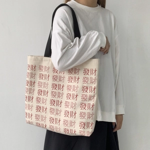 Detail of cream canvas tote bag with red character print and black shoulder straps