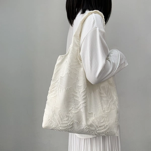 Detail view of the textured ivory leaf embroidery on a canvas shoulder tote bag
