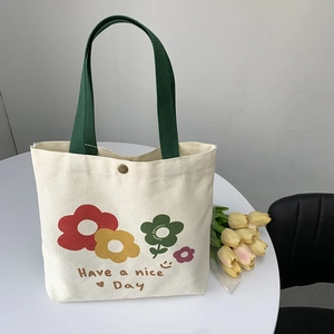 Dettaglio della borsa tote in tela con stampa floreale, manico verde e bottone in metallo