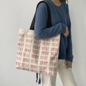 Detailed view of canvas tote bag featuring red Chinese character print and black strap