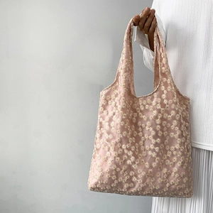 Detail of pink canvas tote bag featuring delicate white daisy embroidery and lace texture