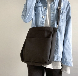 Detail of minimalist black canvas crossbody bag with adjustable strap on denim jacket
