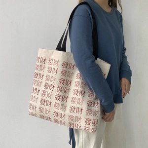 Detail of cream canvas tote bag with red Chinese character print and black strap on model