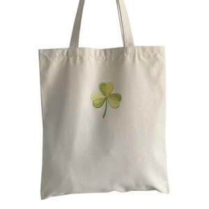 Off-white canvas tote bag featuring a green clover print and dual shoulder straps