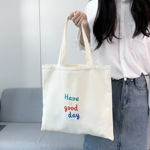 Detail of white canvas tote bag featuring colorful Have a good day lettering and sturdy straps