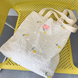 Detailed close-up of daisy embroidery and pink hand-made label on white canvas tote bag