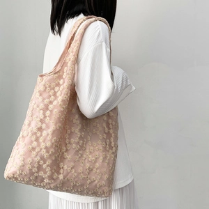Detailed view of pink mesh tote bag with daisy embroidery on model shoulder