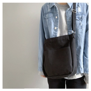 Detail of minimalist black canvas crossbody bag featuring adjustable strap and front pocket