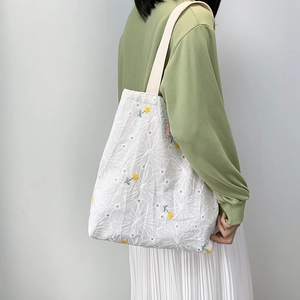Detail of floral embroidery on a white canvas tote bag worn with a casual outfit