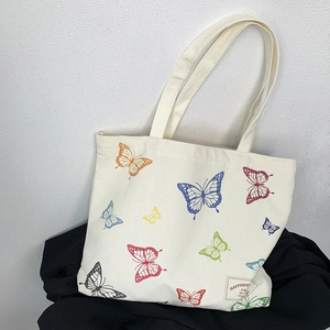Detail of off-white canvas tote bag featuring colorful butterfly prints and stitched label