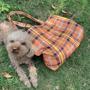 Vue de dessus d'un grand sac cabas à carreaux orange sur l'herbe avec un chiot