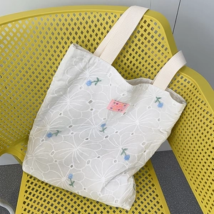 Detail of floral hollow-out embroidery and blue flower accents on white canvas tote bag