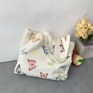 Detailed close-up of a white canvas tote bag featuring colorful butterfly patterns and a text label