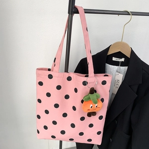 Detail of pink canvas tote bag with black polka dots and orange plush charm hanging on rack