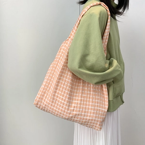 Detail of large capacity orange and white checkered canvas tote bag worn on shoulder