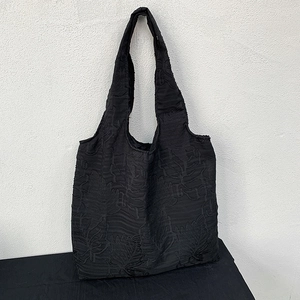 Close-up of black jacquard tote bag with textured leaf patterns and wide shoulder strap