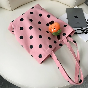 Detailed view of a pink polka dot canvas tote bag with an orange plush fruit charm