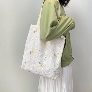 Detailed close-up of embroidered daisy lace pattern on a white canvas tote bag