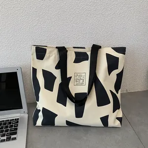 Detail of canvas tote with cow print and Good Student patch next to a laptop