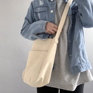 Detail of a cream canvas crossbody bag with side pocket shown on a casual blue denim jacket