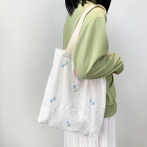 Detail of floral embroidery and eyelet hollow craft on a white canvas tote bag