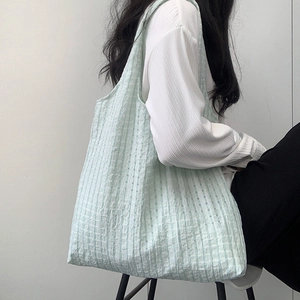 Detail of light green plaid canvas tote bag with textured fabric on model shoulder