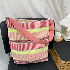 Detailaufnahme der handgewebten Strohtasche mit buntem Streifenmuster und Herz-Label