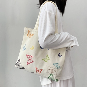 Detailed view of colorful butterfly prints on a beige canvas tote bag worn by a model