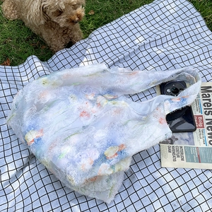Close-up of a white textured floral canvas tote bag on a picnic mat in a garden