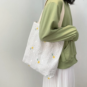 Detail of floral hollow embroidery on white canvas tote bag with yellow accents