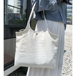 Detailed close-up of white grid textured fabric and metal button on canvas tote bag