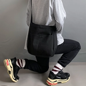 Detail view of a minimalist black canvas crossbody bag with large front pocket and strap