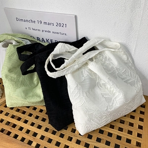 Close-up of three textured tote bags in green, black and white on a wooden bench