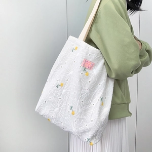 Close-up of white lace tote bag featuring yellow floral embroidery and handmade label